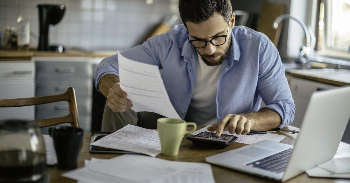 A man sitting at his kitchen table with a calculator and bills.