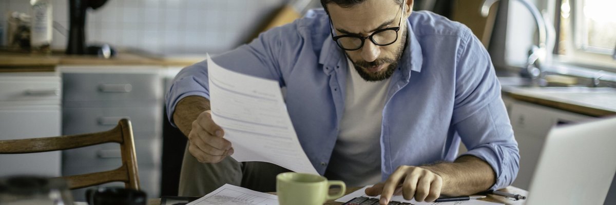 A man sitting at his kitchen table with a calculator and bills.
