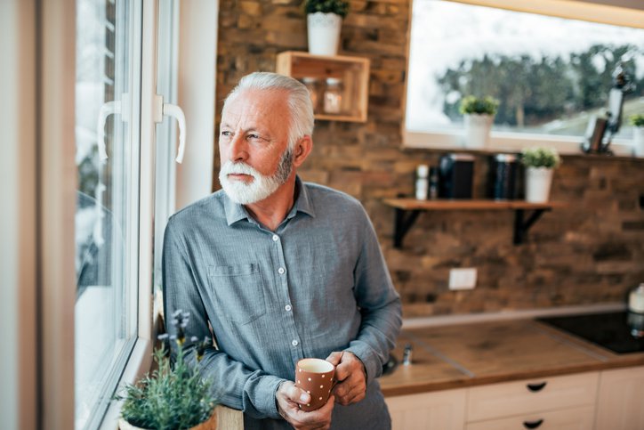 A man holding a cup of coffee and looking out his kitchen window.