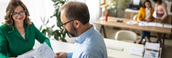 A man speaking with a female financial advisor across a desk in a bank.