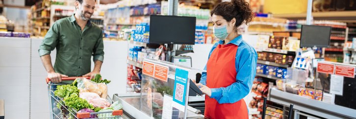 A man pushing a full grocery cart up to the cashier's register.