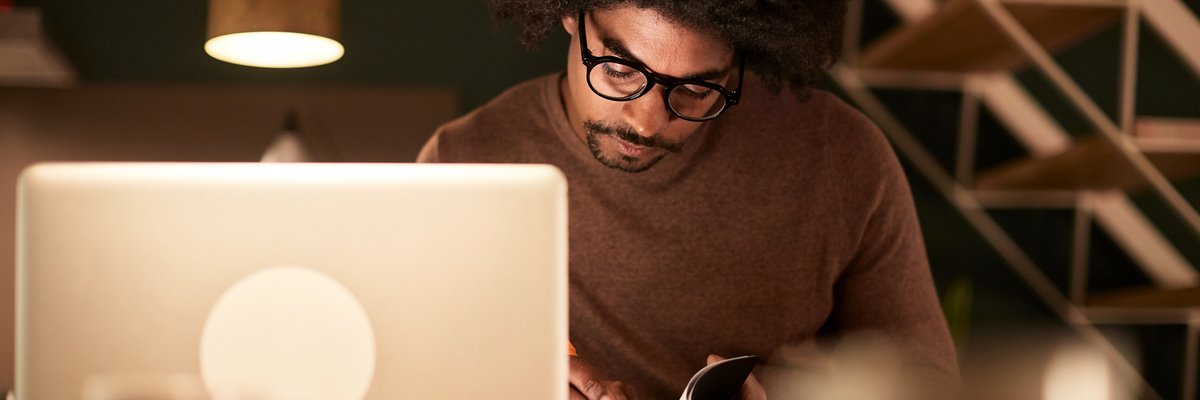 A man sitting with a laptop and notebook late at night.
