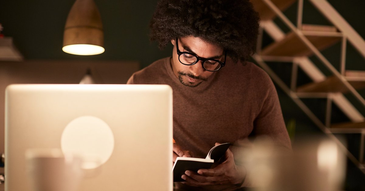 A man sitting with a laptop and notebook late at night.