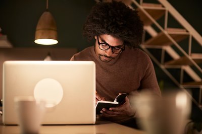 A man sitting with a laptop and notebook late at night.