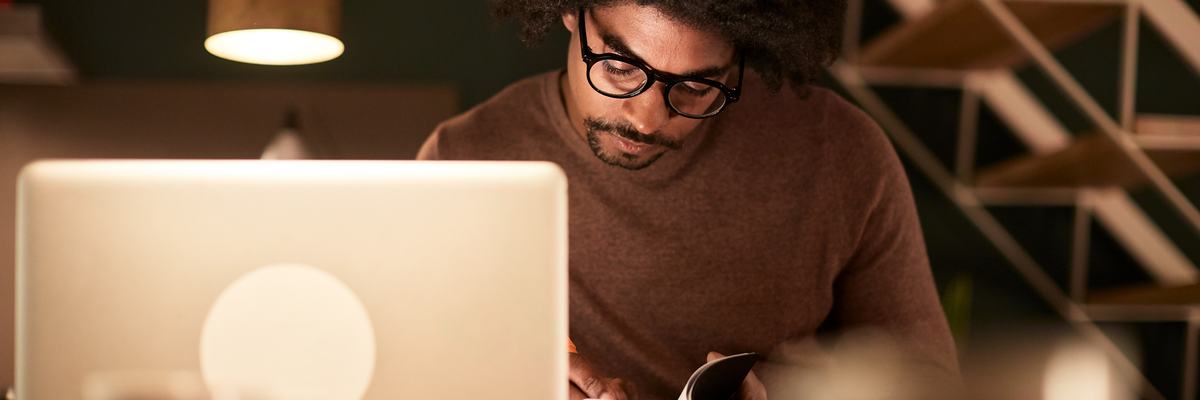 A man sitting with a laptop and notebook late at night.