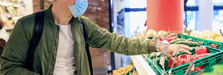A young man wearing a medical mask while shopping for produce at a grocery store.