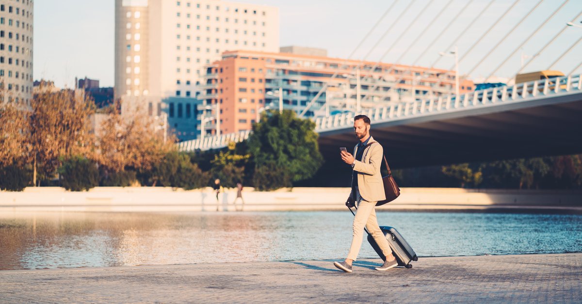A person with a suitcase walking along a river in the middle of a city.