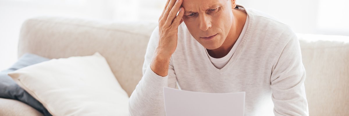 An adult male rubbing his temple as he looks at paperwork.