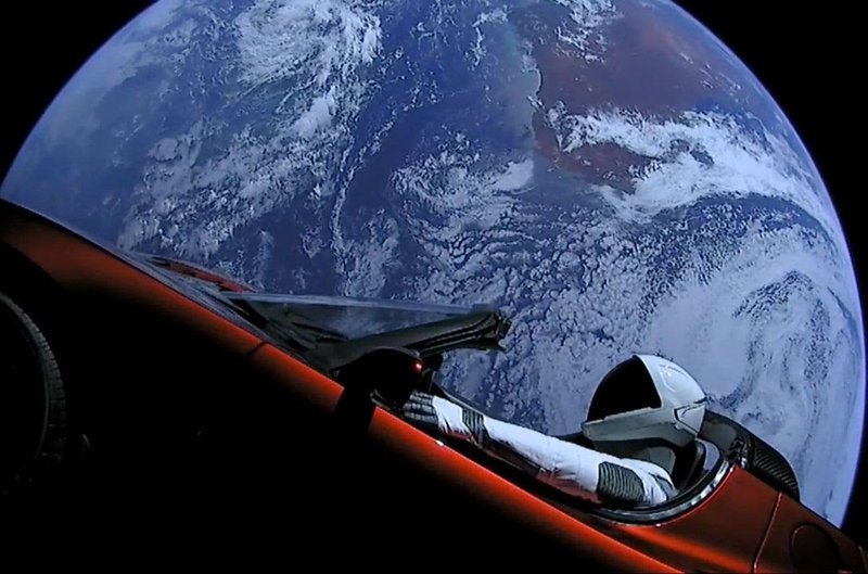 Tesla advertisement with picture of an astronaut in a red Tesla with Earth in the background.