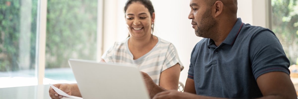 A couple smile while looking at paperwork together at the kitchen table.