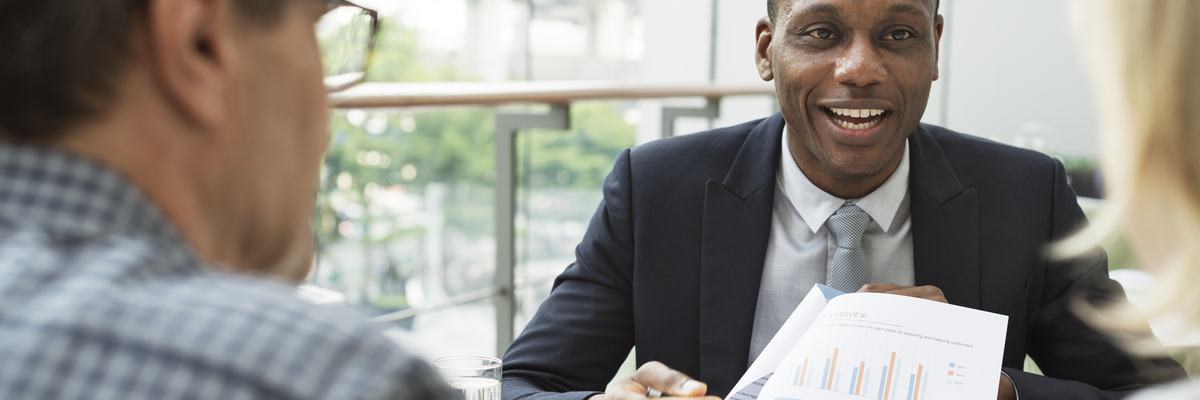 mature man and woman sitting at desk talking to man in business suit