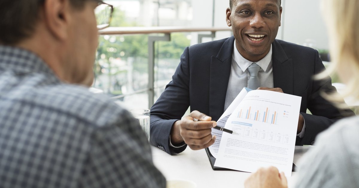 mature man and woman sitting at desk talking to man in business suit
