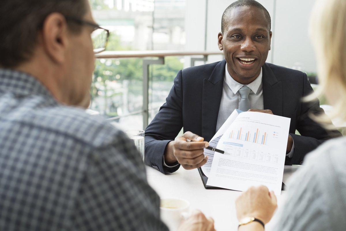 mature man and woman sitting at desk talking to man in business suit