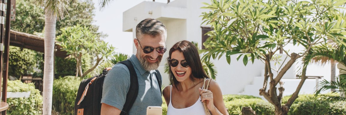 mature man and woman taking a selfie in front of a hotel and palm trees
