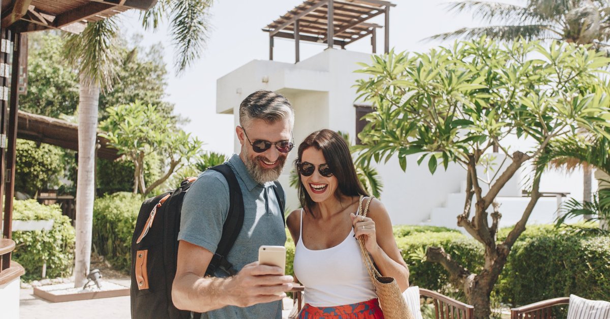 mature man and woman taking a selfie in front of a hotel and palm trees