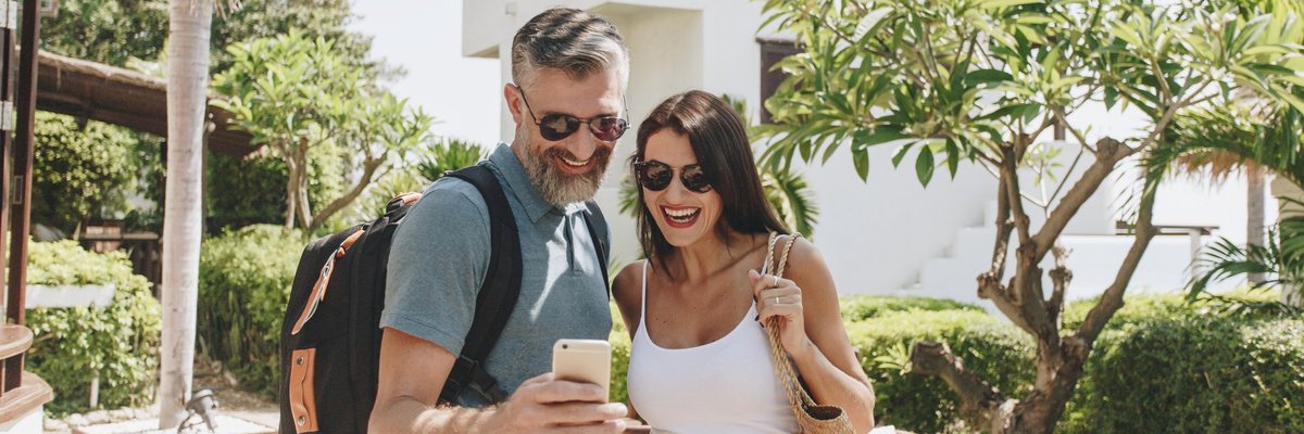 mature man and woman taking a selfie in front of a hotel and palm trees