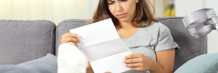 A woman with a cast on her leg looks at a medical bill