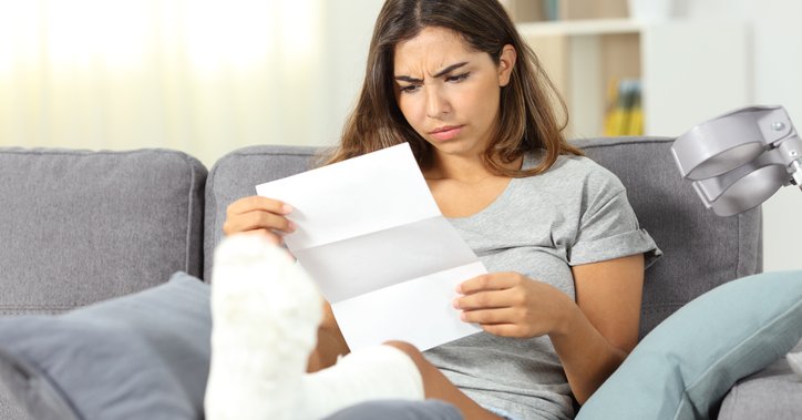 A woman with a cast on her leg looks at a medical bill