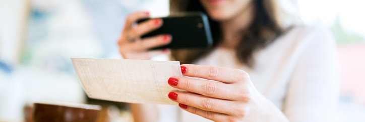A young woman takes a picture of a check with her phone.