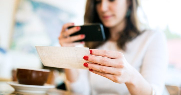 A young woman takes a picture of a check with her phone.