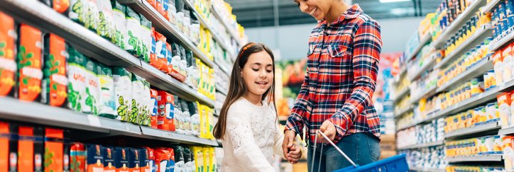 A mom and daughter walking down the aisle of a grocery and putting food in their basket.
