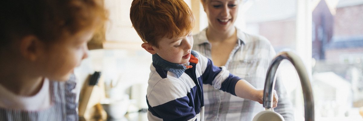 A mom and her two young children washing dishes in a bright kitchen.