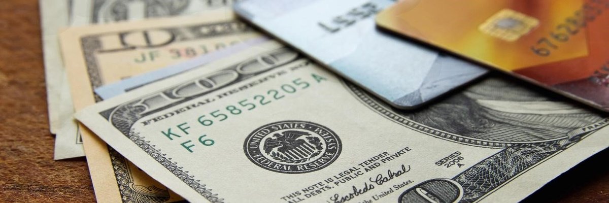 Two credit cards sitting on top of various American dollars.