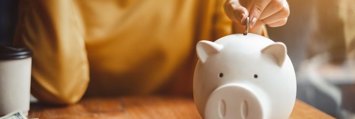 Someone puts coins into a piggy bank.