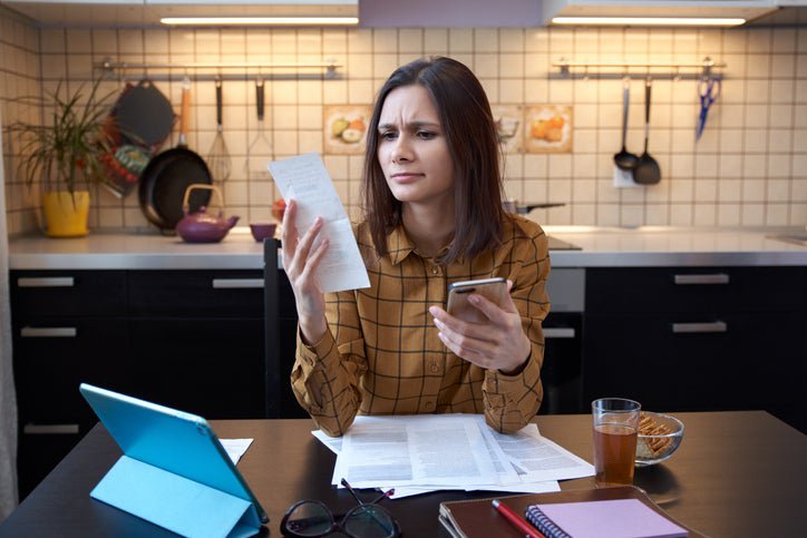 A frowning woman with bills, a calculator, and a tablet.