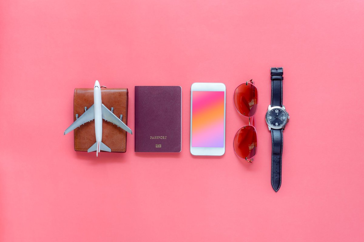 A wallet, toy airplane, passport, phone, sunglasses, and watch on a pink background.
