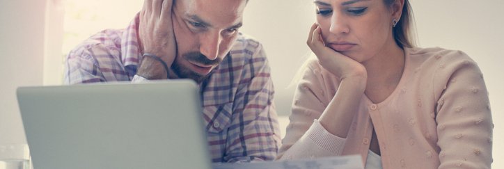 A worried man and woman looking at bills and a laptop