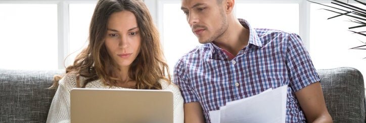 A couple looking worried about money, with a laptop and bills.