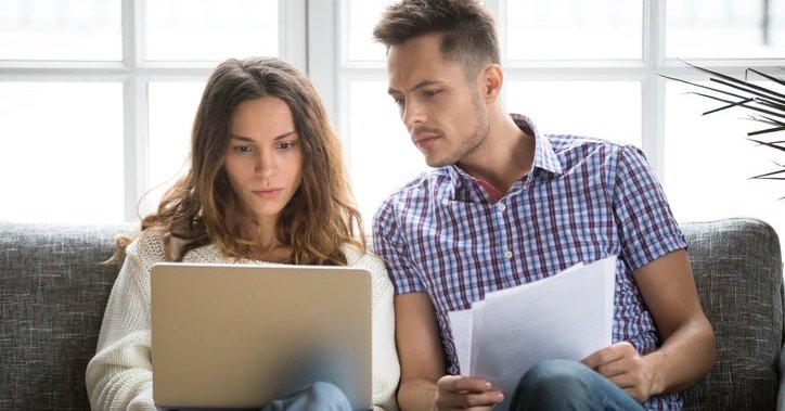 A couple looking worried about money, with a laptop and bills.