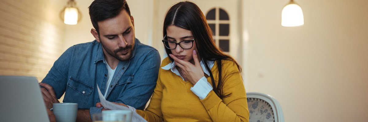 Couple eating breakfast looking at papers and laptop confused.
