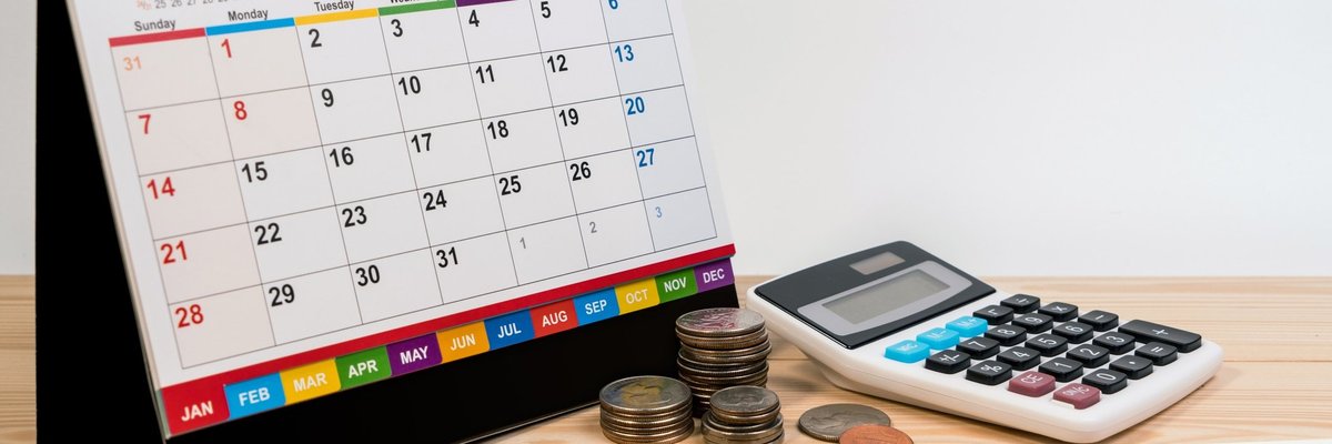 A spiral bound desk calendar turned to January sitting beside coins, a calculator, and writing utensils.