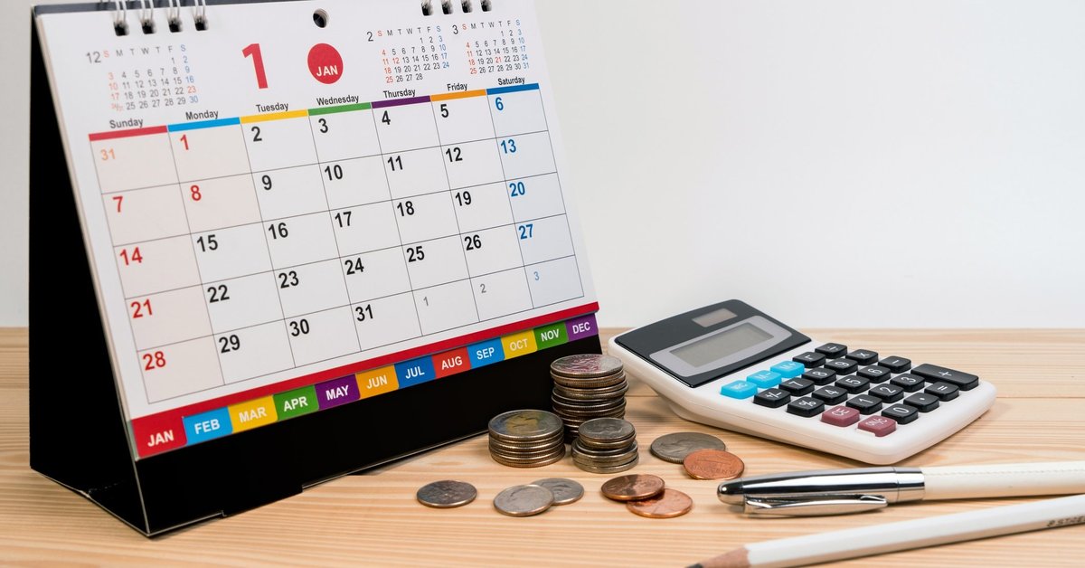 A spiral bound desk calendar turned to January sitting beside coins, a calculator, and writing utensils.