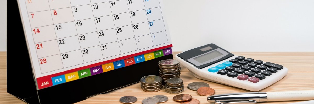 A spiral bound desk calendar turned to January sitting beside coins, a calculator, and writing utensils.