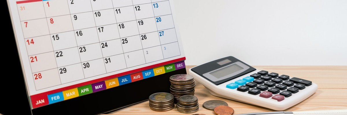 A spiral bound desk calendar turned to January sitting beside coins, a calculator, and writing utensils.