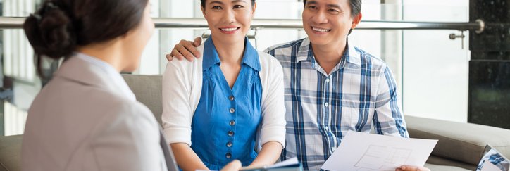 A smiling couple talking to a woman who is showing them a tablet.