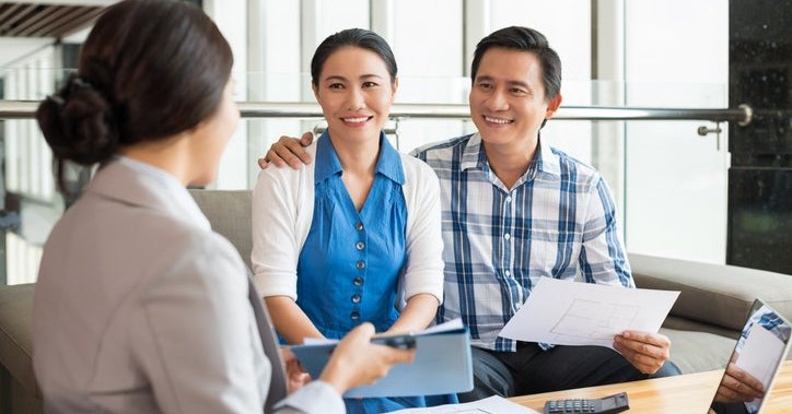 A smiling couple talking to a woman who is showing them a tablet.