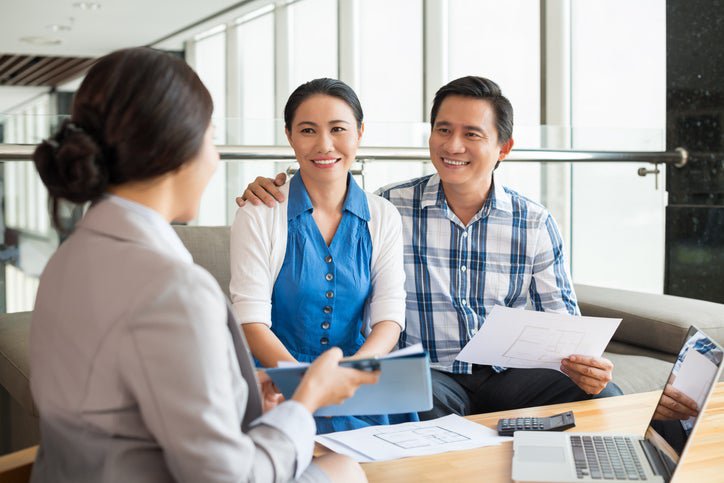 A smiling couple talking to a woman who is showing them a tablet.