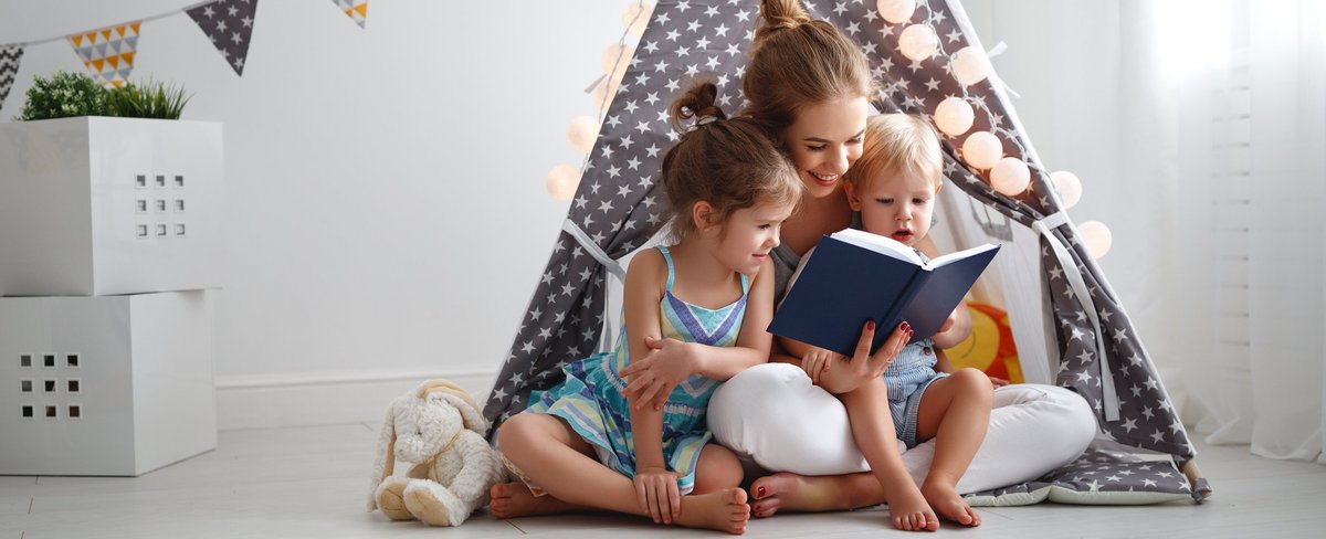 A mother reading to two young children in a fort.
