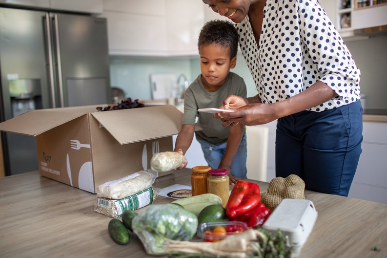 A mother and her young son unpacking the groceries from a meal service kit in their kitchen.