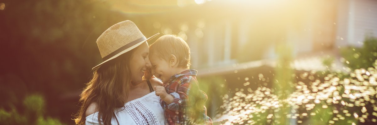 A mother holding her young son while watering plants in the backyard.