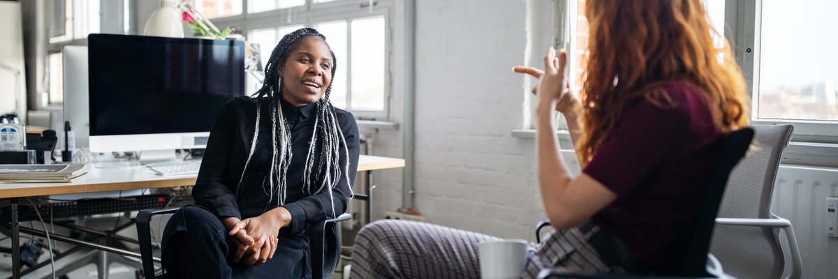 Two office employees chatting with each other from their desks.
