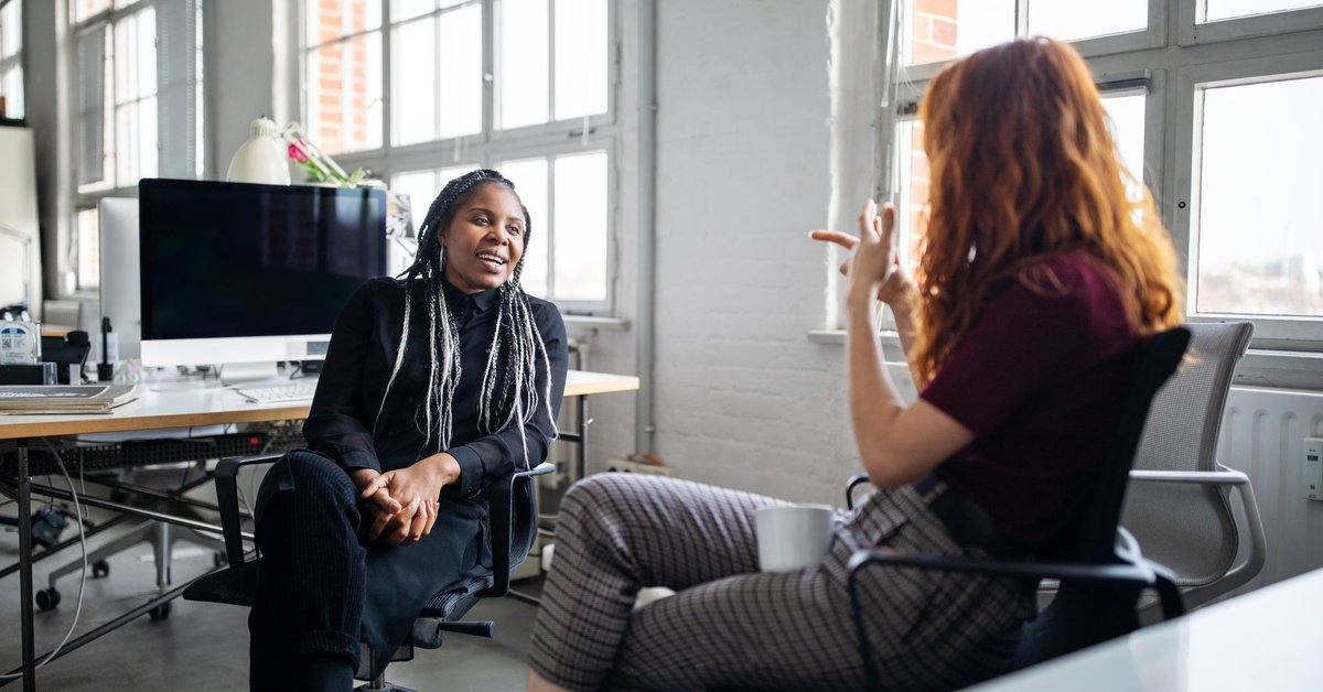 Two office employees chatting with each other from their desks.