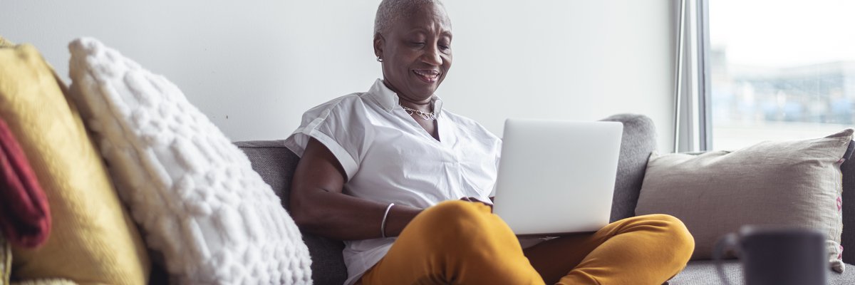 An older adult sitting crosslegged on the couch while typing on a laptop.