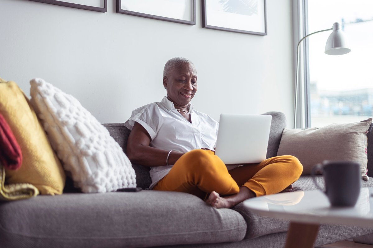 An older adult sitting crosslegged on the couch while typing on a laptop.