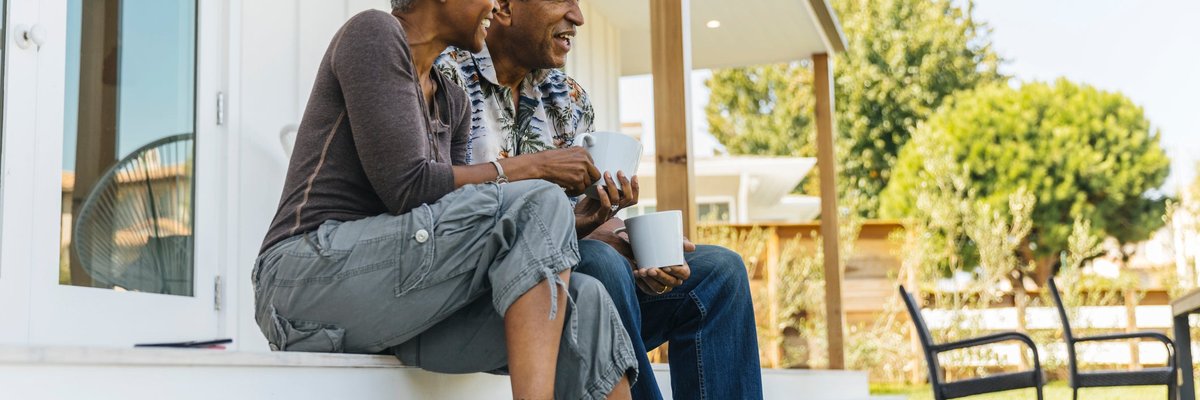 An older couple sit on their back porch, sip coffee, and enjoy the morning.