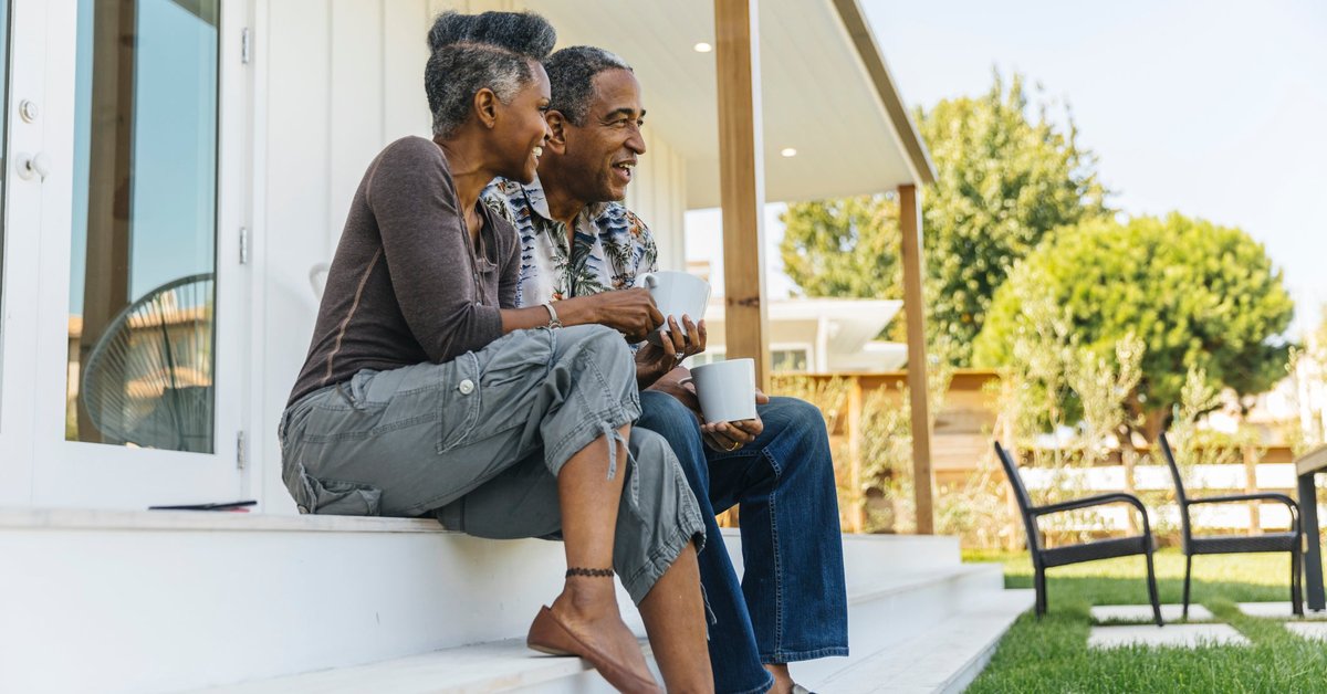 An older couple sit on their back porch, sip coffee, and enjoy the morning.